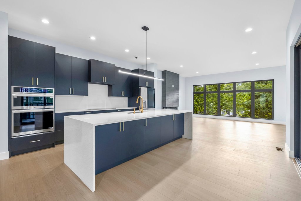 Modern kitchen with large white island and blue cabinets, open to family room with large windows.